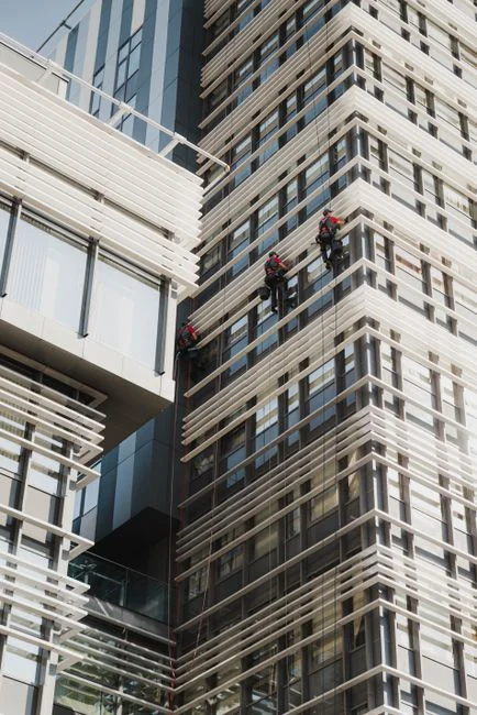 A man cleaning a glass barrier outdoors with a squeegee, surrounded by greenery.